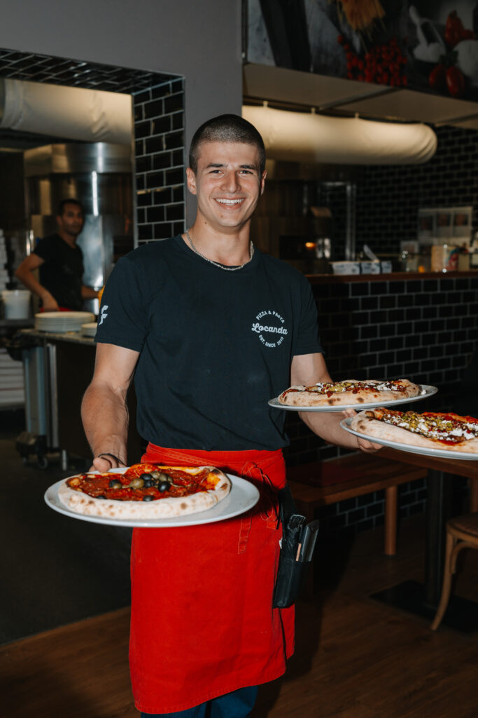 Locanda Mitarbeiter serviert lächelnd Pizzen