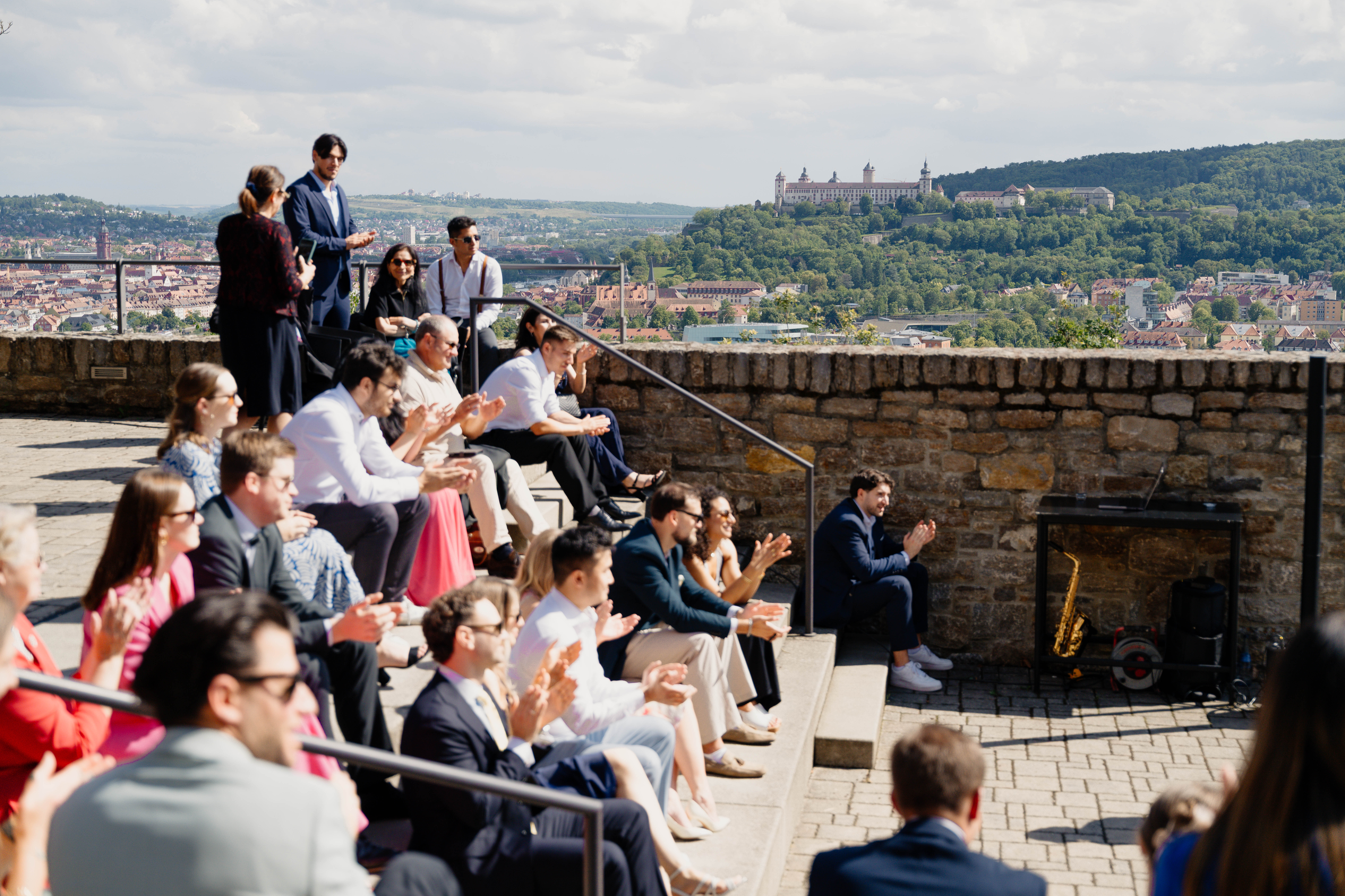 Hochzeitsgäste applaudieren auf einer Tribüne des Schlosshotels Steinburg. Im Hintergrund ist die Festung Marienberg zu sehen.