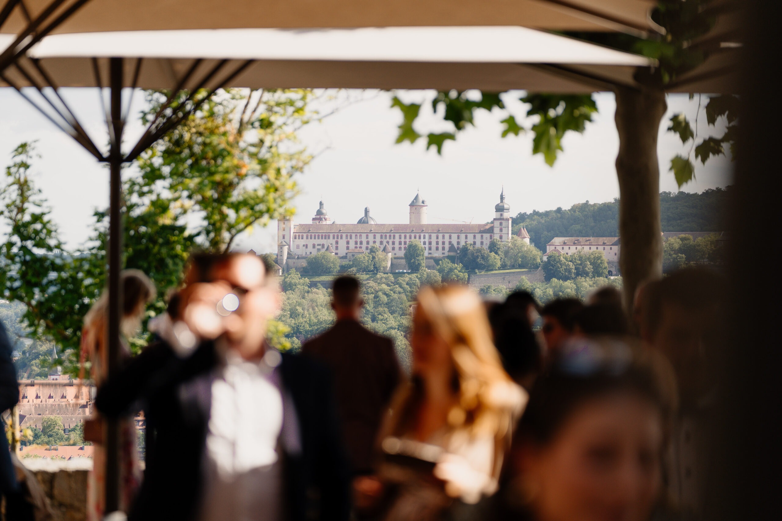 Eine Hochzeitsgesellschaft blickt von dem Schlosshotel Steinburg auf die Festung Marienberg in Würzburg.